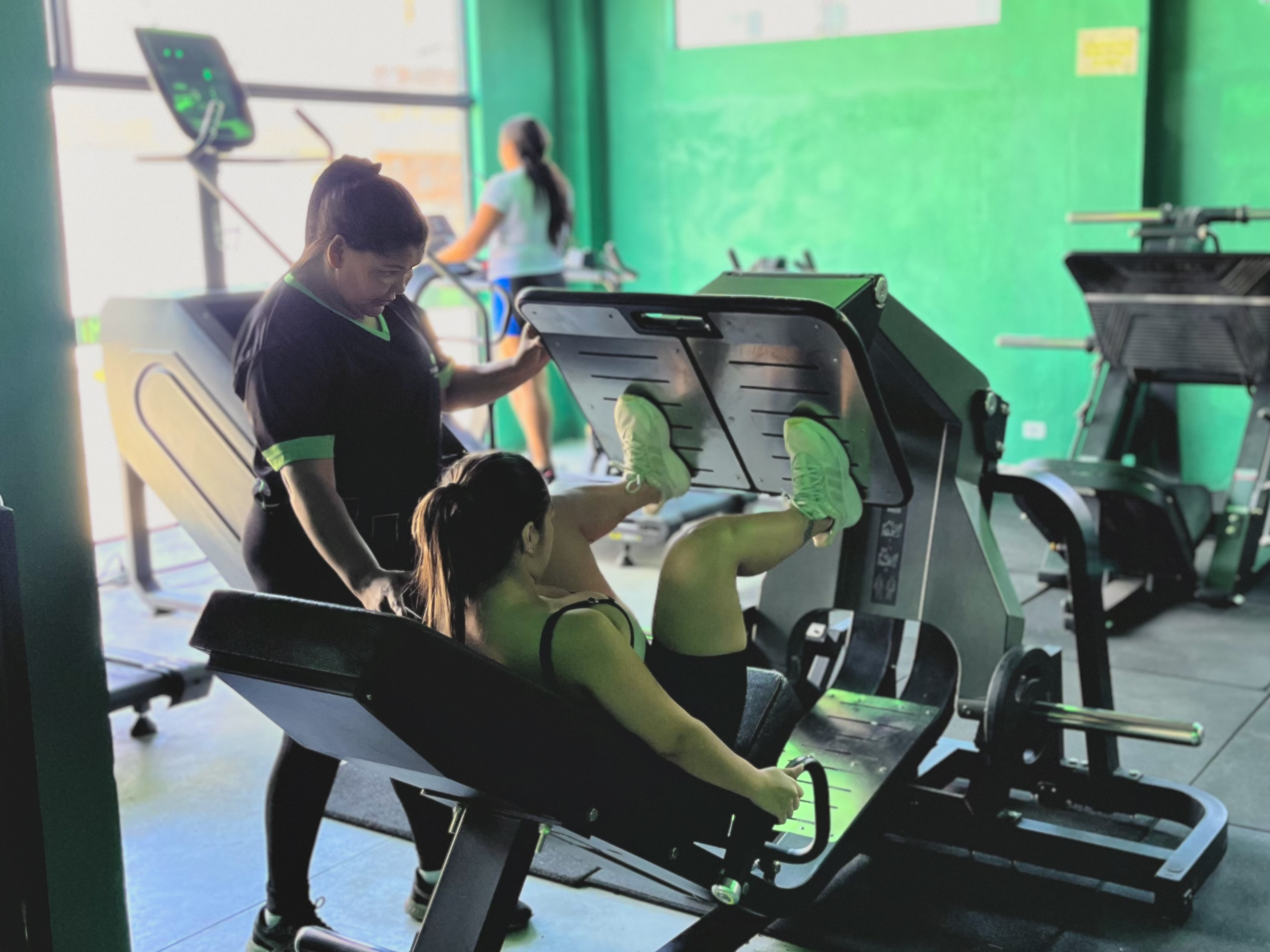 Treinadora auxiliando aluno, focada na execução correta.